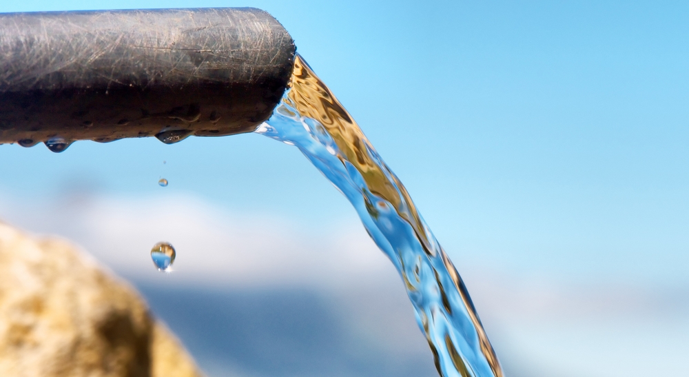 Water flowing from pipe against blurred mountains